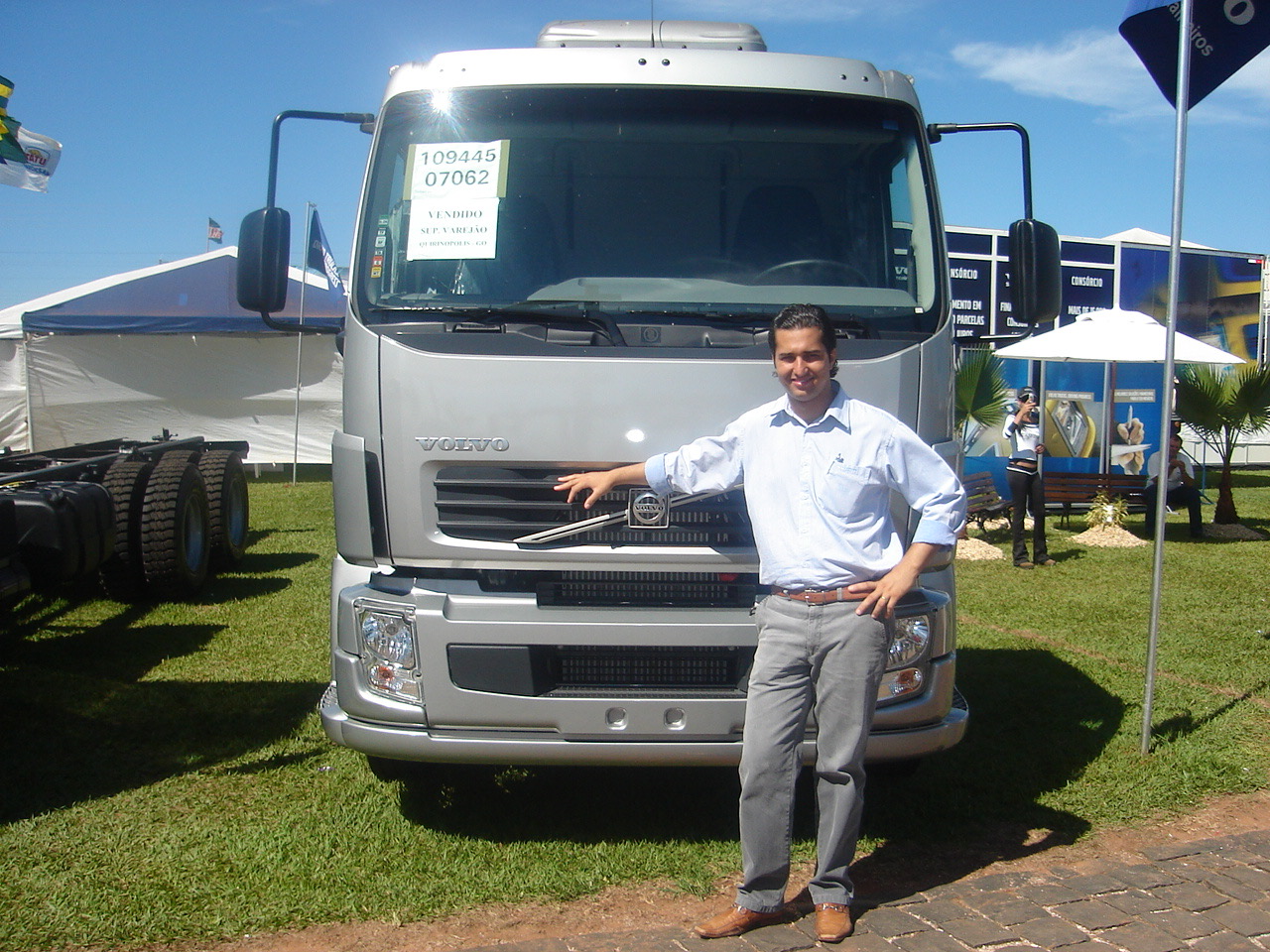 Jonathas de camisa branca ao lado de um caminhão Volvo prateado com aviso VENDIDO no para-brisa