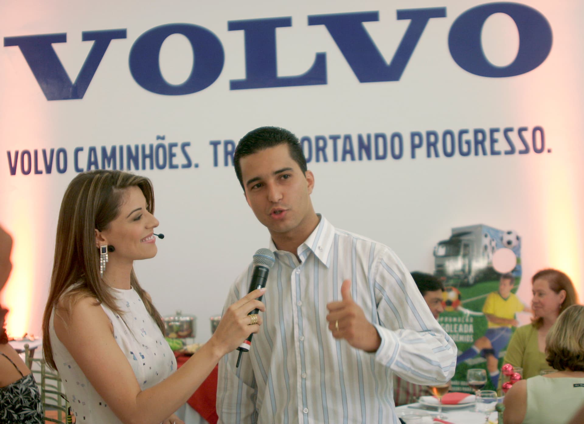 Jonathas falando ao microfone ao lado de uma apresentadora diante de um painel Volvo