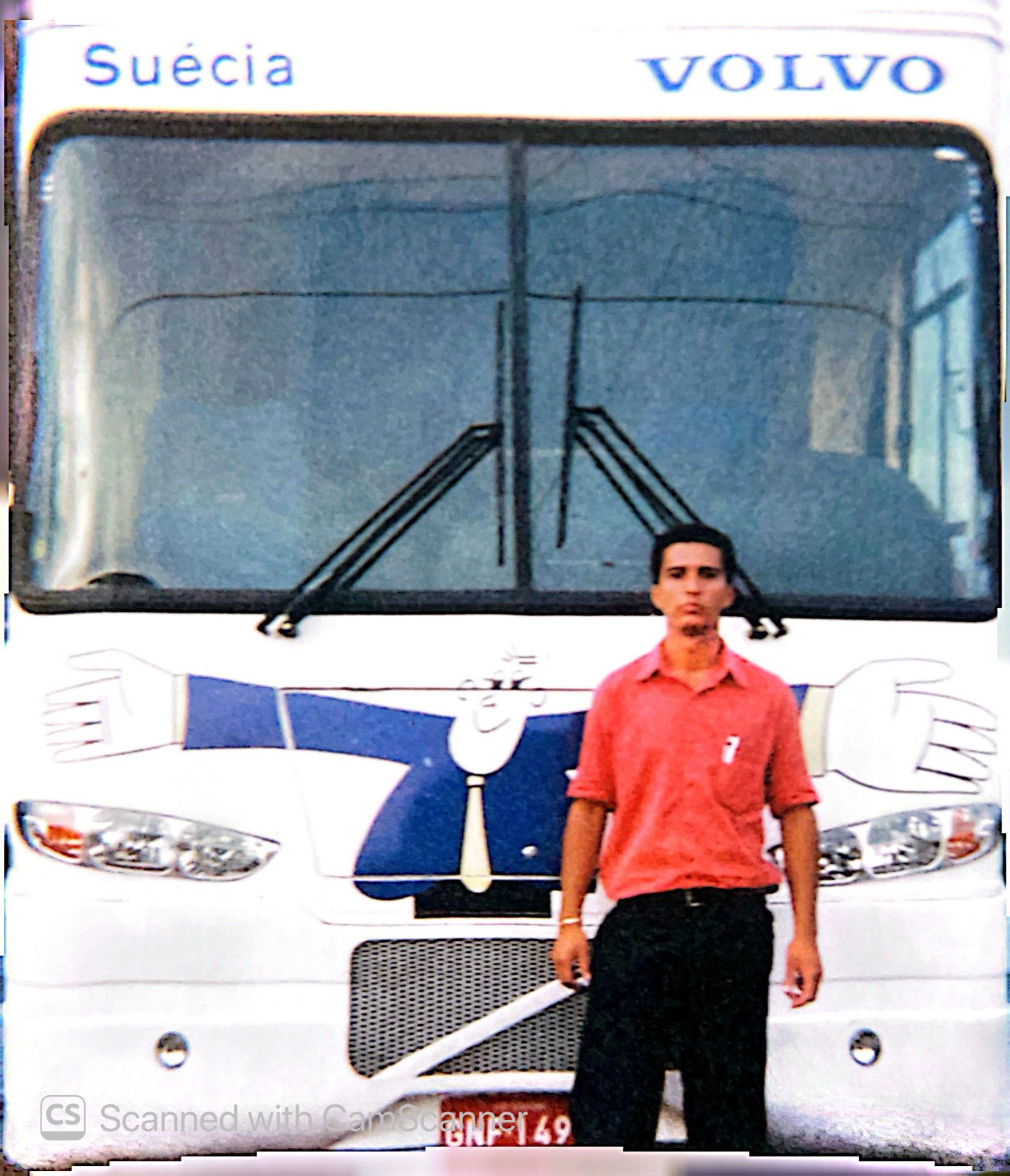 Jonathas jovem de camisa alaranjada em frente a um ônibus