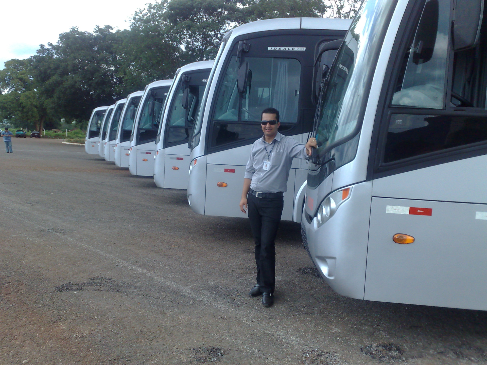 Jonathas em pé ao lado de vários ônibus em um pátio